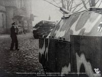 Das Bild zeigt zwei auf dem Kopfsteinpflaster vor dem Bahnhofsgeb&auml;ude vorbeifahrende Jagdpanzer IV (V) L/70.